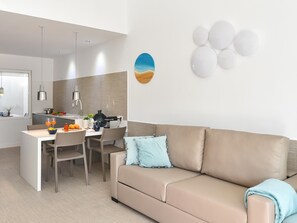 A modern living room with a beige sofa, a dining table with chairs, and a kitchen area in the background.