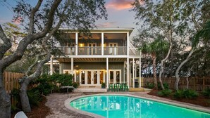 A two-story house with a pool, surrounded by trees and a wooden fence.