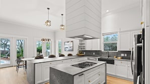 A modern kitchen with a large island, white cabinetry, and a built-in stove.