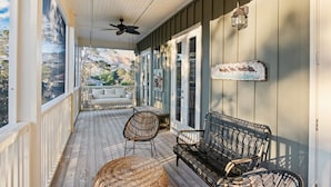 A covered porch with a ceiling fan, wicker furniture, and a view of the surrounding landscape.
