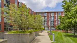 Un bâtiment moderne avec un chemin en béton, des espaces verts aménagés et un ciel dégagé.