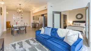 Un appartement moderne comprenant un canapé bleu, un coin repas, une kitchenette et une chambre avec un lit et une table de chevet.
