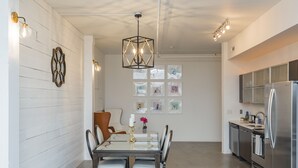 Une cuisine moderne dotée d’appareils électroménagers en acier inoxydable, un coin repas avec une table et des chaises en verre, et des œuvres d’art décoratives sur les murs.