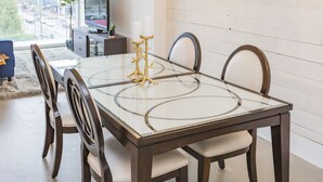 Une table à manger avec un plateau en verre et quatre chaises, un chandelier doré et un téléviseur en arrière-plan.