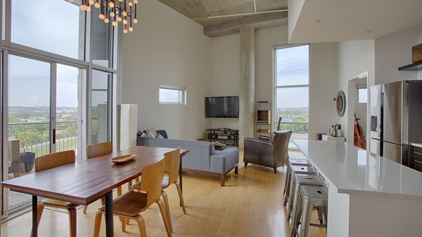 A modern kitchen with a large island, a dining area with a wooden table and chairs, and a living room with a sofa and TV. - Luxe Downtown Penthouse with City Skyline Views (Nashville)