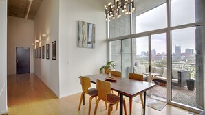 A spacious dining area with a large wooden table and chairs, a modern chandelier, and a city view through large windows. - Luxe Downtown Penthouse with City Skyline Views (Nashville)