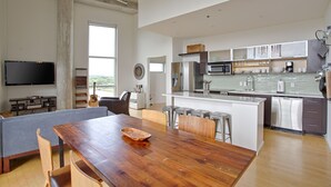 A modern kitchen with a central island, stainless steel appliances, and a dining area with a wooden table and chairs. - Luxe Downtown Penthouse with City Skyline Views (Nashville)