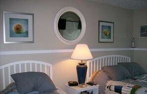 A bedroom with two beds, a nightstand with a lamp, and framed pictures on the wall.