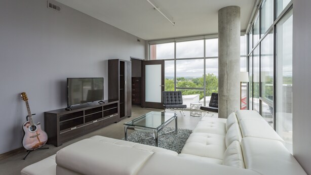 Un salon moderne avec un canapé blanc, une table basse en verre, un téléviseur posé sur un meuble sombre et une guitare appuyée contre le mur.