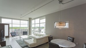 Un salon spacieux doté d’une grande fenêtre, d’un canapé blanc, d’une table à manger avec des chaises et d’un luminaire suspendu.