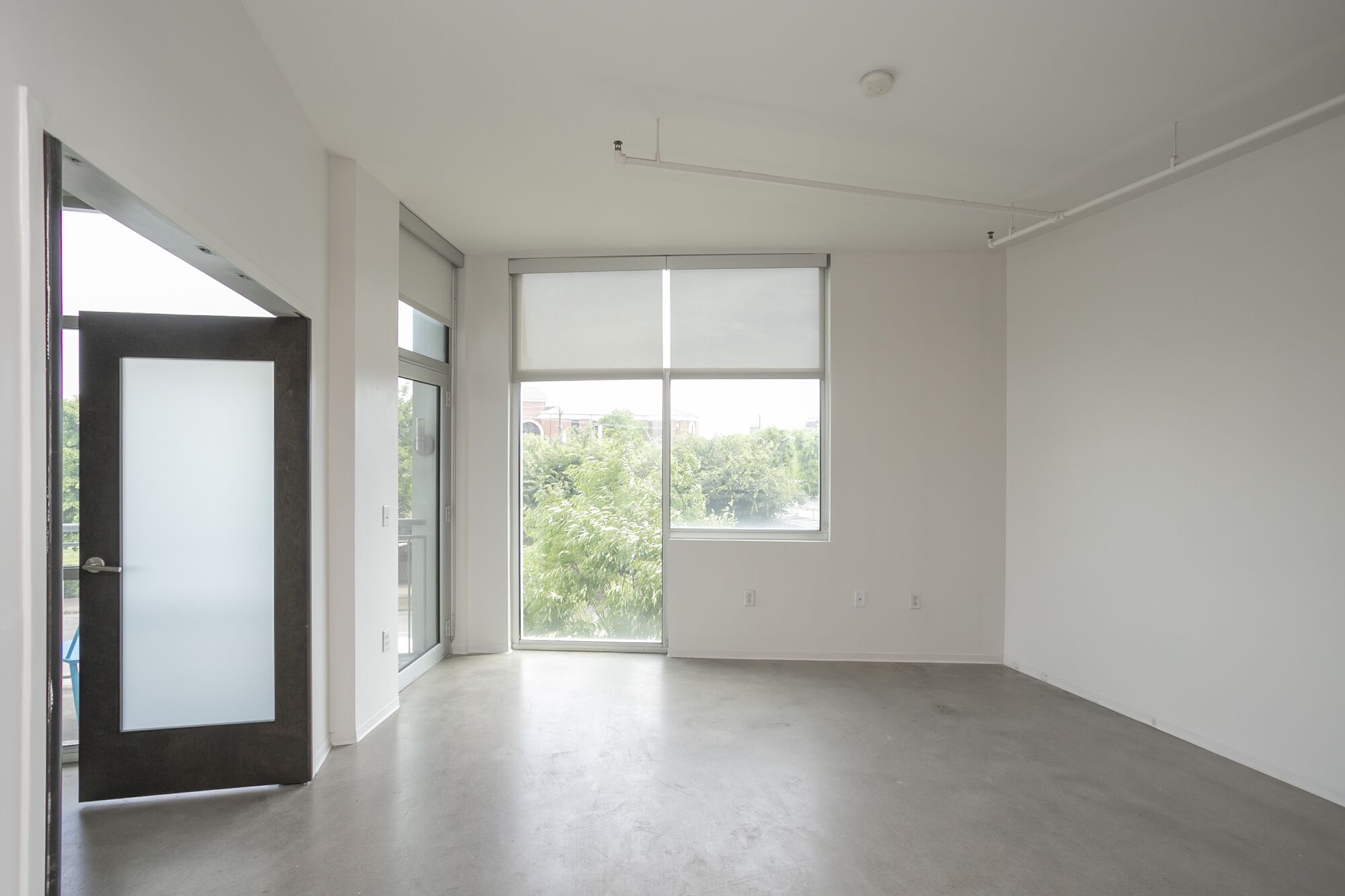 A spacious, empty room with a large window, a door, and a concrete floor.
