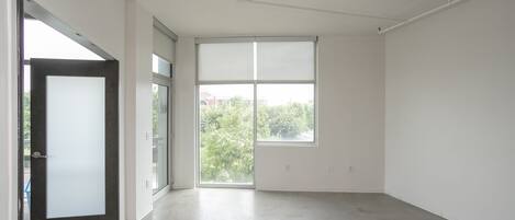 A spacious, empty room with a large window, a door, and a concrete floor.