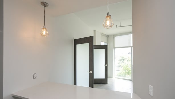 Un baño moderno con un mostrador blanco, dos lámparas colgantes, una puerta que da a otra habitación y un ventanal.