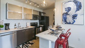 Cocina moderna con electrodomésticos de acero inoxidable, una isla blanca y taburetes rojos.