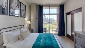Un dormitorio con una cama grande, vistas de la ciudad desde un balcón y cuadros en la pared.
