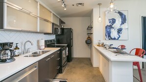 Una cocina moderna con electrodomésticos de acero inoxidable, una encimera blanca y una zona de comedor con una silla roja.