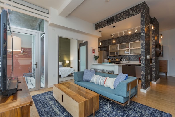 A modern living room with a sofa, coffee table, and a kitchen area visible through an open door. - Artsy Extended Retreat Downtown Nashville (Nashville)
