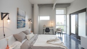 Un dormitorio moderno con una cama grande, un escritorio y una silla. Hay una ventana que proporciona luz natural y vistas al exterior.