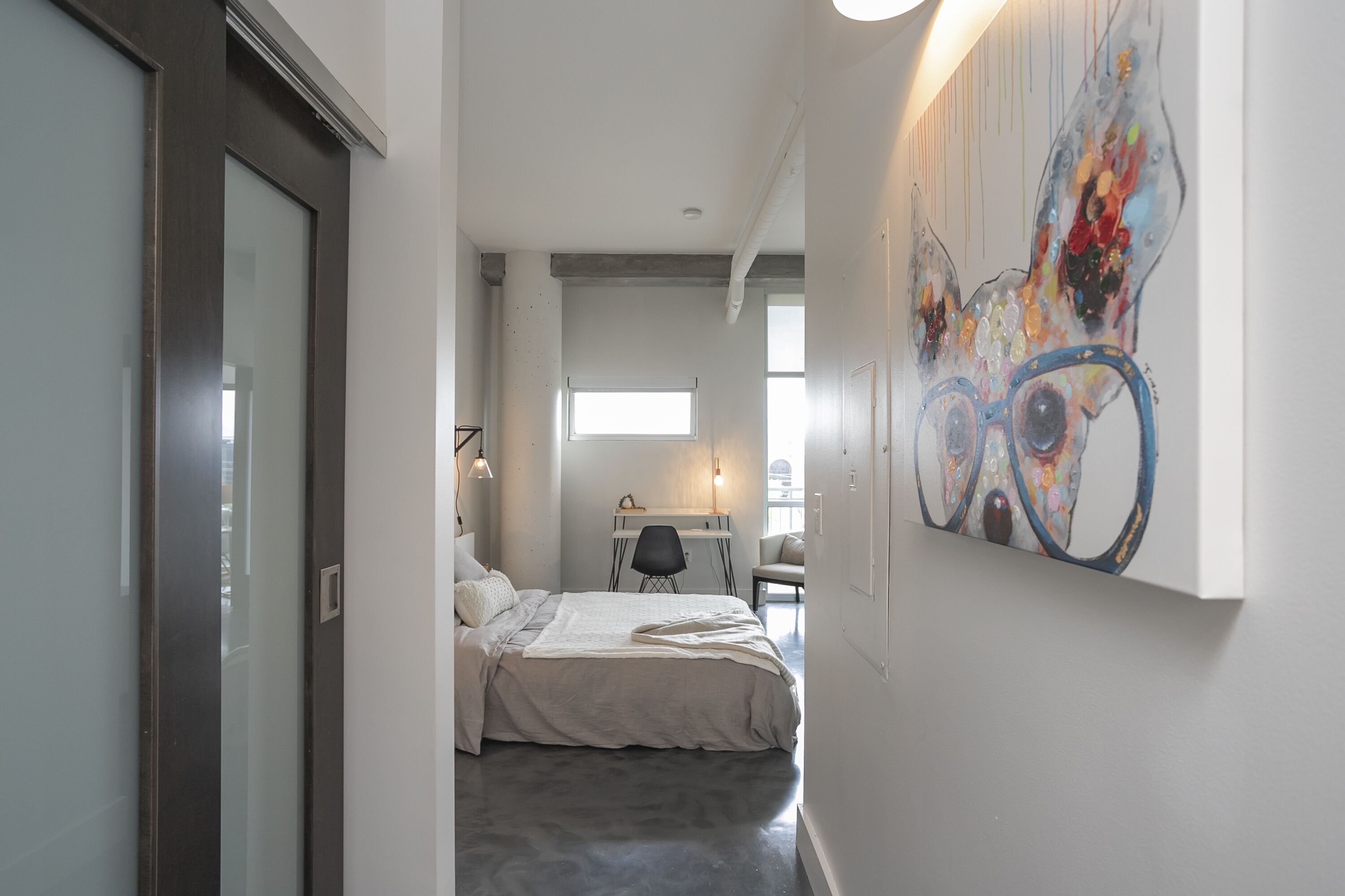 A narrow hallway leading to a bedroom with a bed, a desk, and a chair.