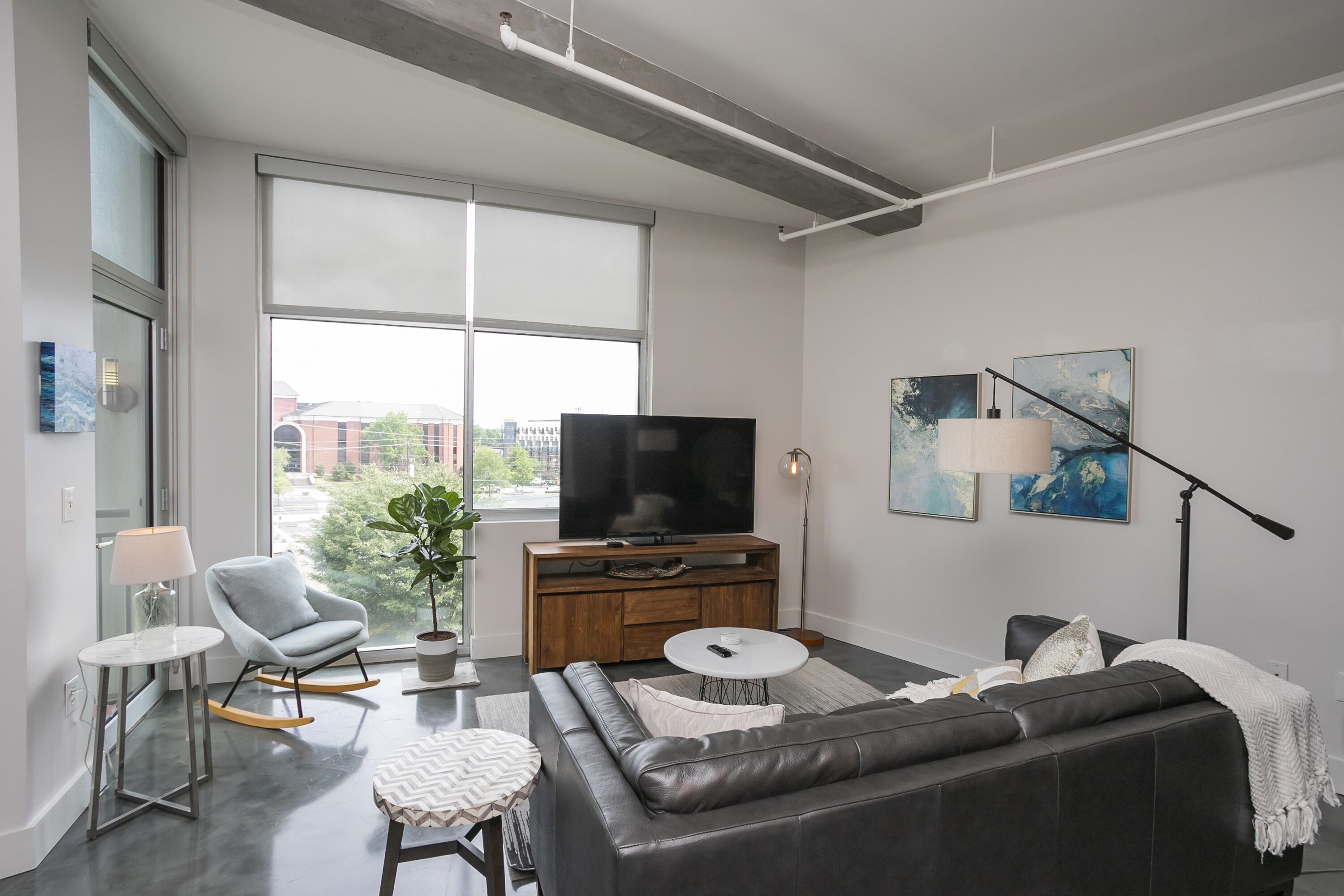 A modern living room with a large window, a flat-screen TV, a sofa, a coffee table, and a floor lamp.