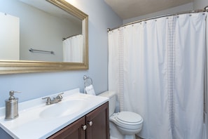 A bathroom with a white sink, two faucets, a mirror, a toilet, and a shower curtain.