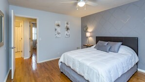 A bedroom with a bed, a ceiling fan, a nightstand, and a wall with artwork.