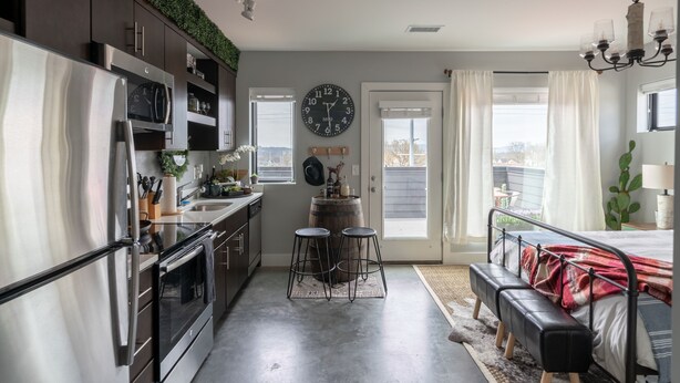 A modern kitchen with a stainless steel refrigerator, a clock, and a bar stool area. - Rustic Luxe Studio Apartment with Rooftop Deck (Nashville)
