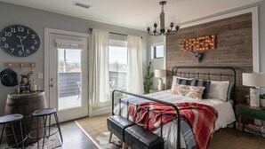 A bedroom with a bed, a chandelier, a clock, a door, and a view of the outdoors. - Rustic Luxe Studio Apartment with Rooftop Deck (Nashville)