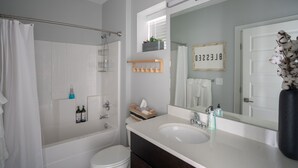 A modern bathroom with a bathtub, toilet, and sink. There is a shower curtain, a towel rack, and a mirror with a sign above it. - Rustic Luxe Studio Apartment with Rooftop Deck (Nashville)