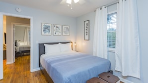 A bedroom with a bed, a ceiling fan, a window with curtains, and a door leading to another room.