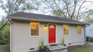 A single-story house with a red door, two windows with yellow-tinted glass, and a small porch area.