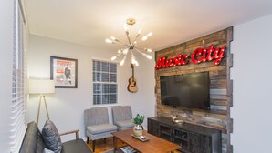 A living room with a sofa, two armchairs, a coffee table, a guitar, a TV, and a neon sign reading "Music City".