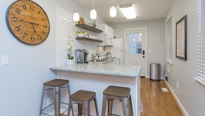 A modern kitchen with a large wooden clock, stainless steel bar stools, and pendant lighting.