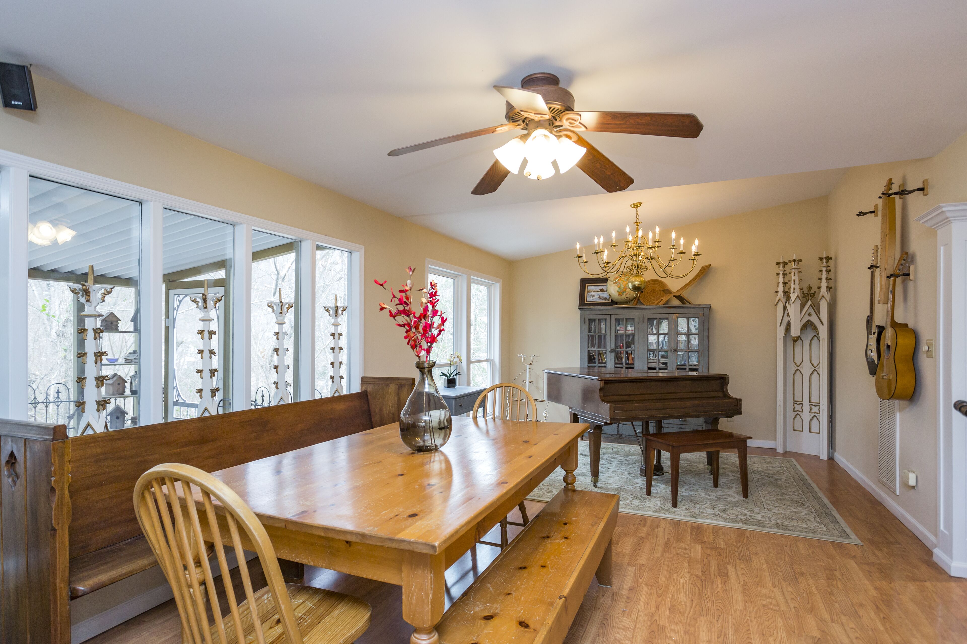 A dining area with a wooden table, benches, a chandelier, a piano, and a violin on the wall.