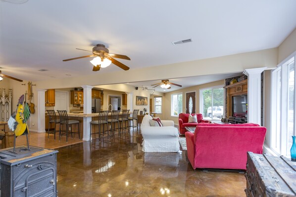 A spacious living area with a polished floor, a red sofa, a white armchair, and a kitchen in the background.