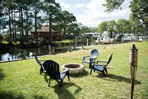 Relax in a serene outdoor setting with Adirondack chairs surrounding a fire pit, overlooking a tranquil body of water.