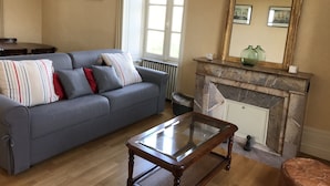 A living room with a blue sofa, a glass-top coffee table, a fireplace, and a large mirror. - Charming cottage on the banks of the Mayenne river (Montreuil-Juigné)