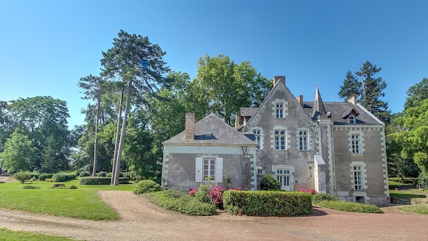 A large, historic stone building with multiple chimneys and windows, surrounded by well-maintained gardens and tall trees. - Charming cottage on the banks of the Mayenne river (Montreuil-Juigné)