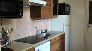 A compact kitchen with wooden cabinets, a microwave, a stove, and a dishwasher. - Charming cottage on the banks of the Mayenne river (Montreuil-Juigné)