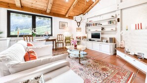 Un salon chaleureux avec un canapé, une table basse et une vue sur un paysage verdoyant grâce à de grandes fenêtres.
