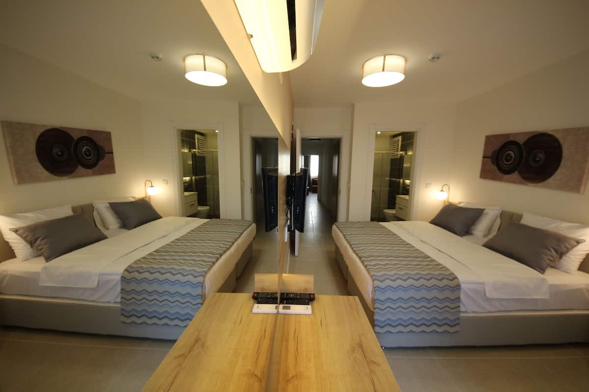 Een hotelkamer met spiegels, twee bedden, een houten tafel en een gang naar een badkamer.