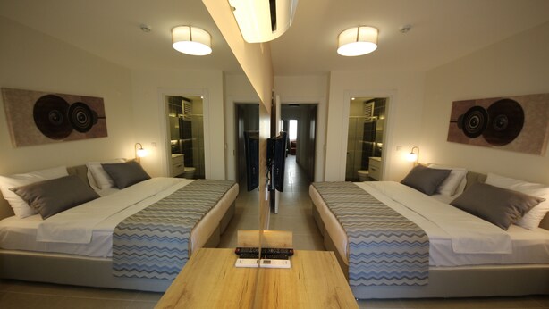 A mirrored room with two beds, a wooden table, and wall-mounted light fixtures. - Spilos Gumuldur Hotel (Menderes)
