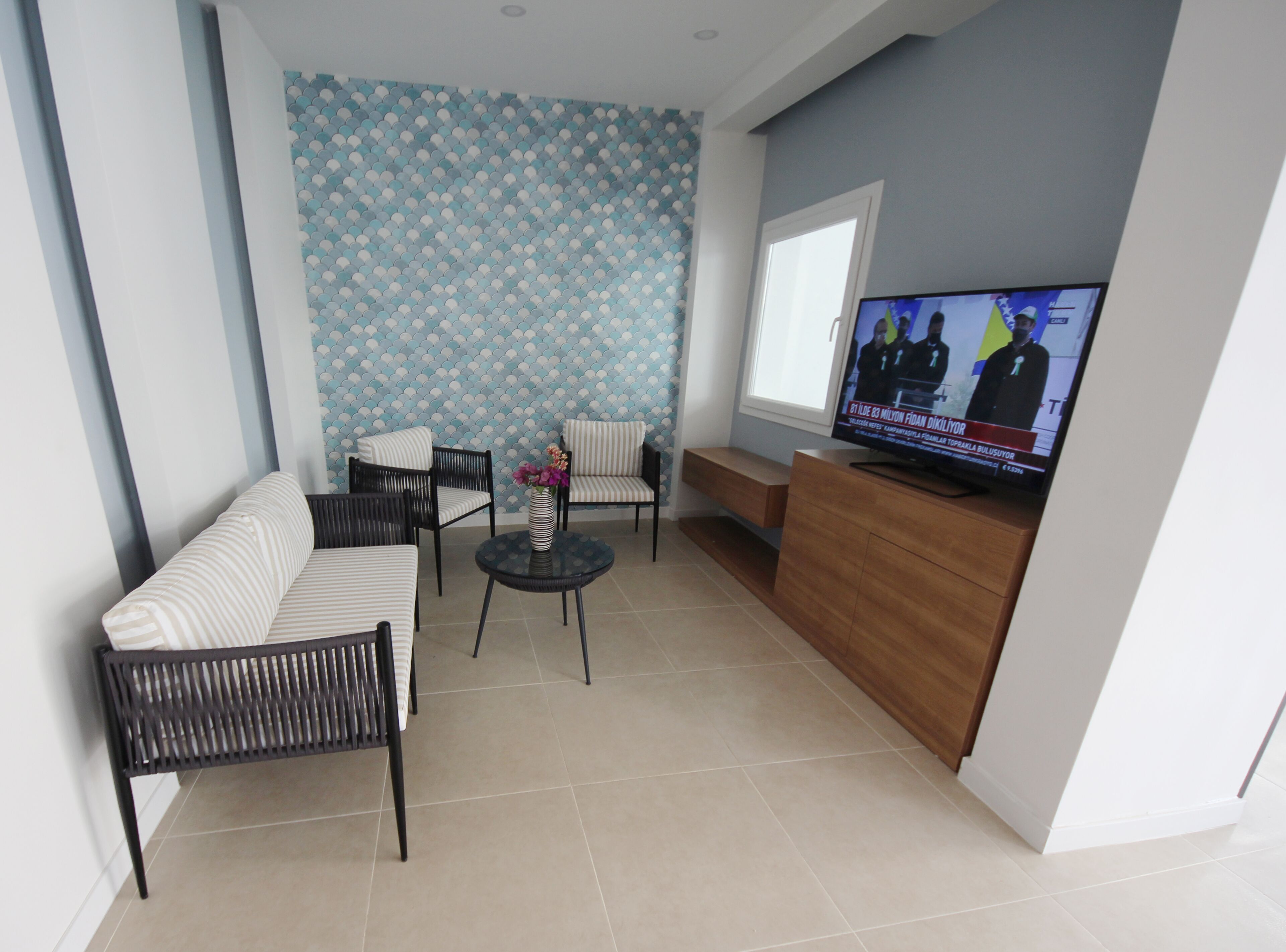 Ein Wohnzimmer mit einer Couch, Sesseln, einem Couchtisch, einem Fernseher und einer Wand mit Muster.