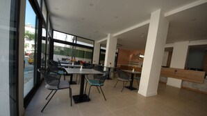 A modern dining area with tables and chairs, large windows, and a view of the street. - Spilos Gumuldur Hotel (Menderes)