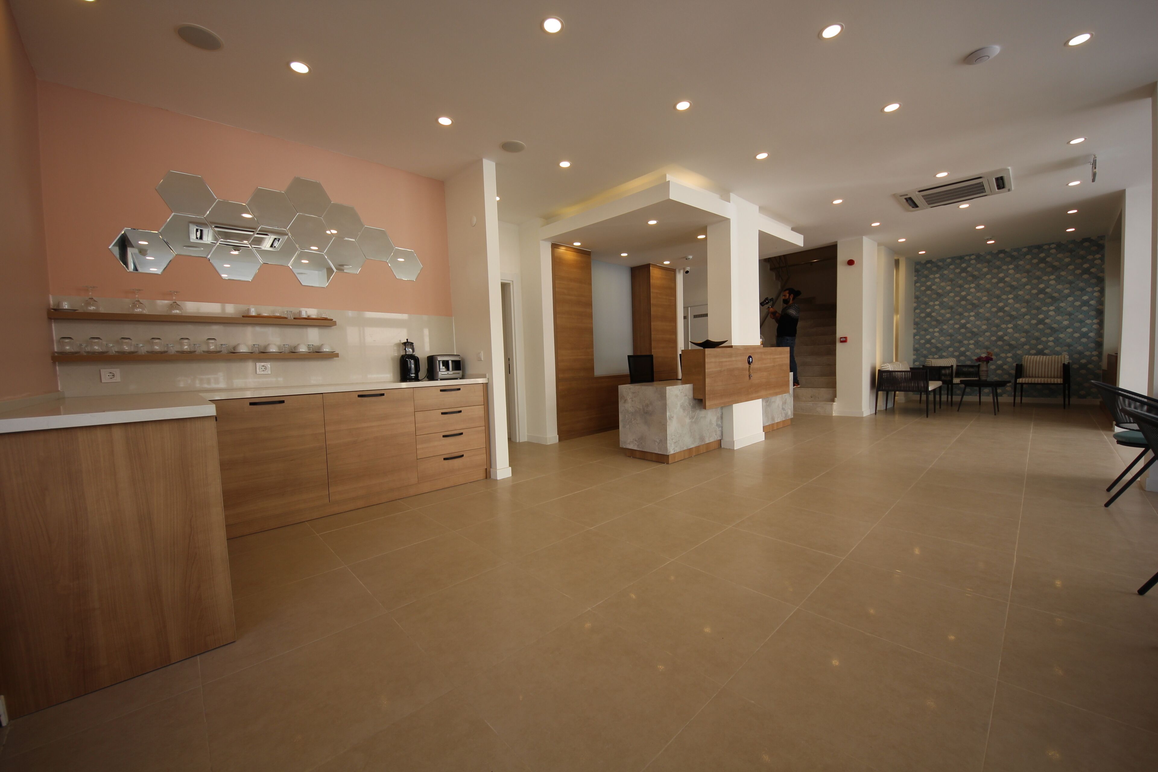 A modern kitchen with wooden cabinets, a countertop, and a hexagonal mirror. There is a seating area with chairs and a table in the background.