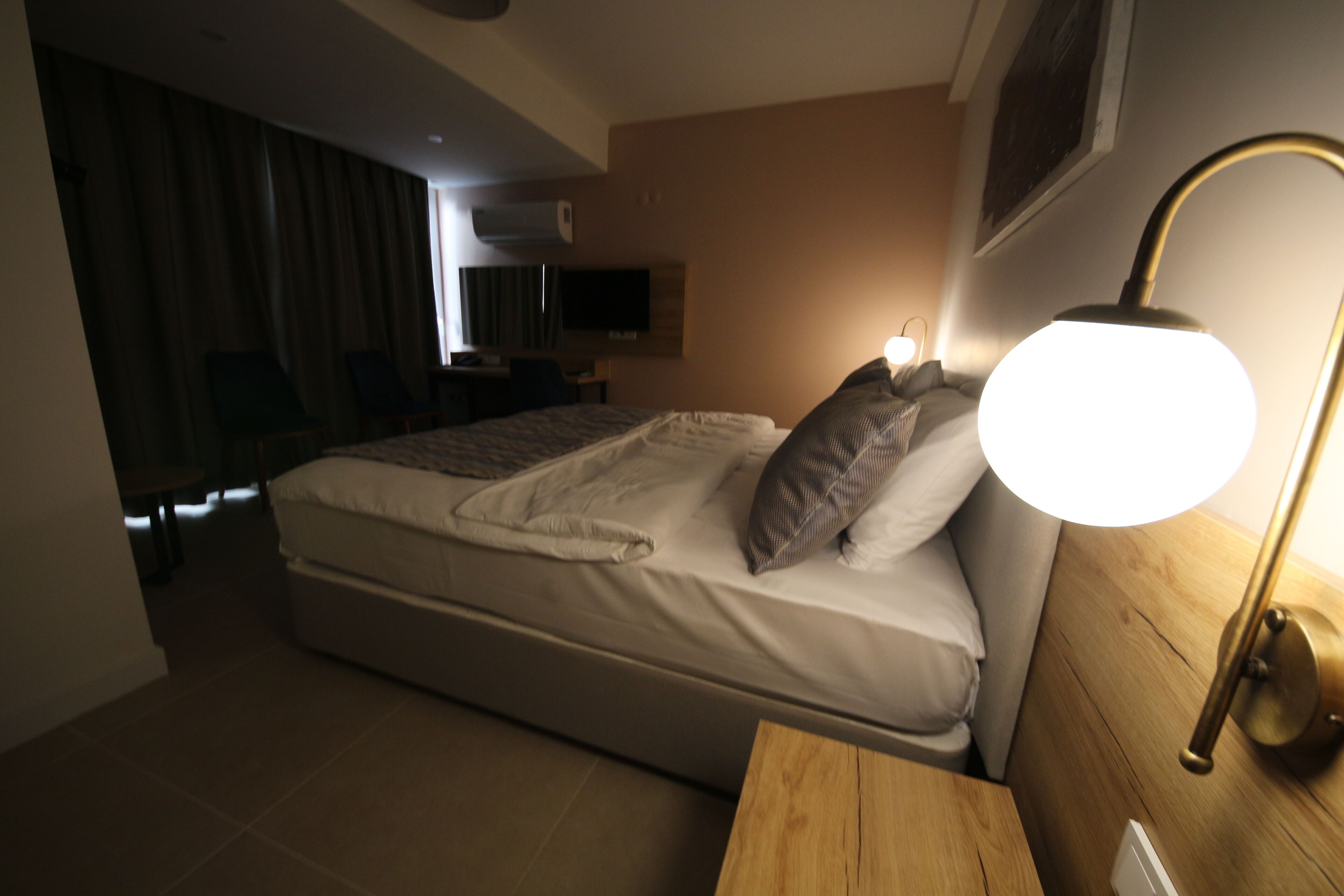 A hotel room with a bed, a bedside table, a lamp, a TV, and a view of the hallway.
