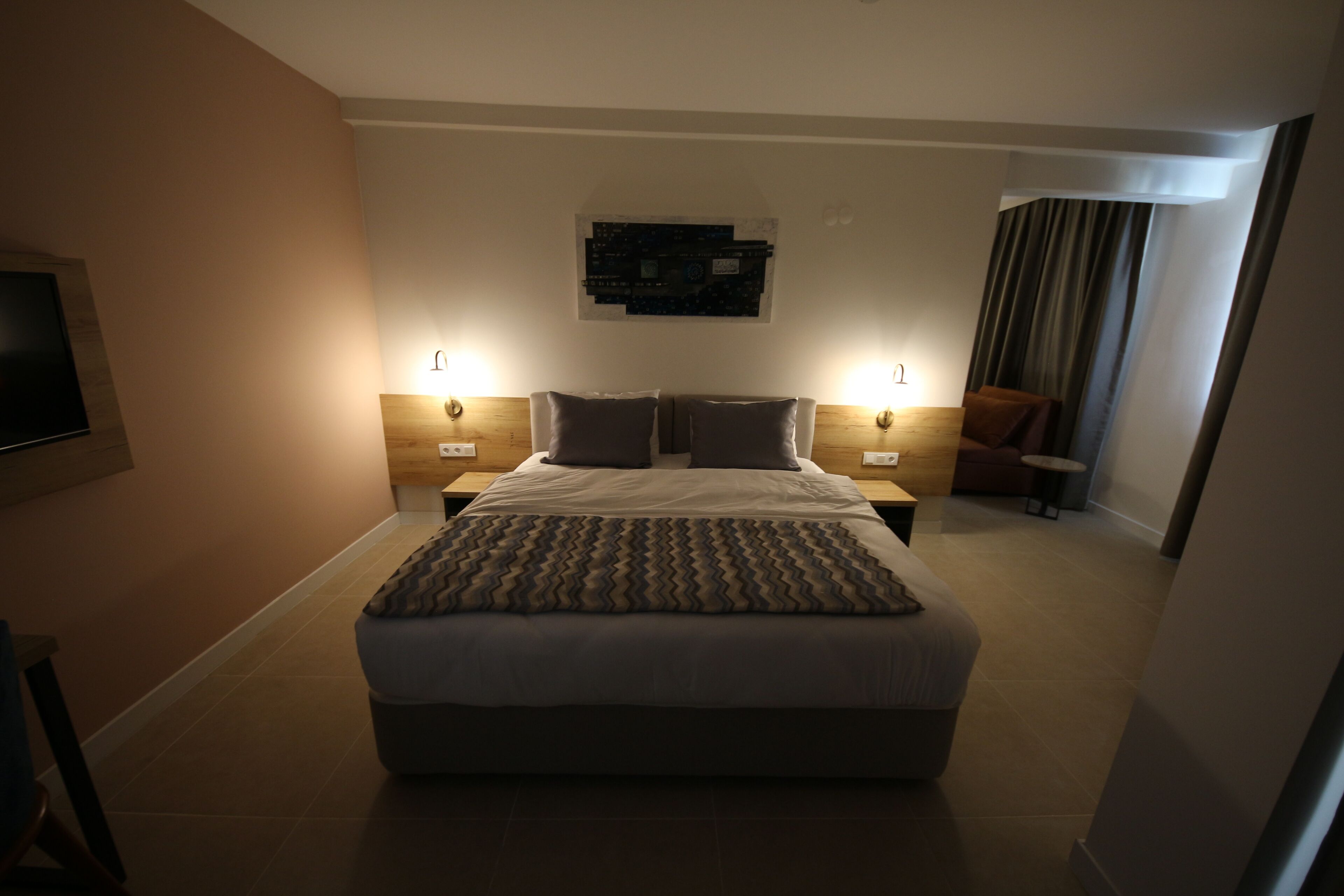 A modern hotel room with a large bed, two bedside tables, a flat-screen TV, and a wall-mounted artwork.