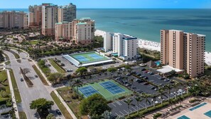A coastal hotel complex with multiple high-rise buildings, a tennis court, and a parking area.