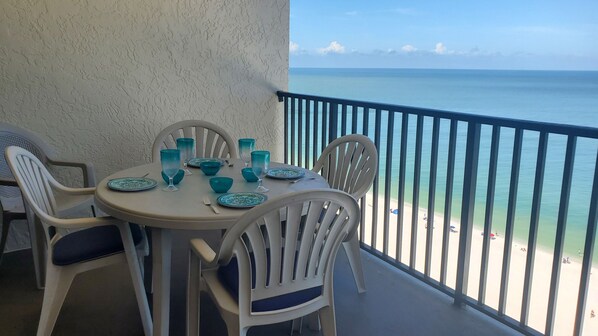 A balcony with a table set for four, overlooking a beach.