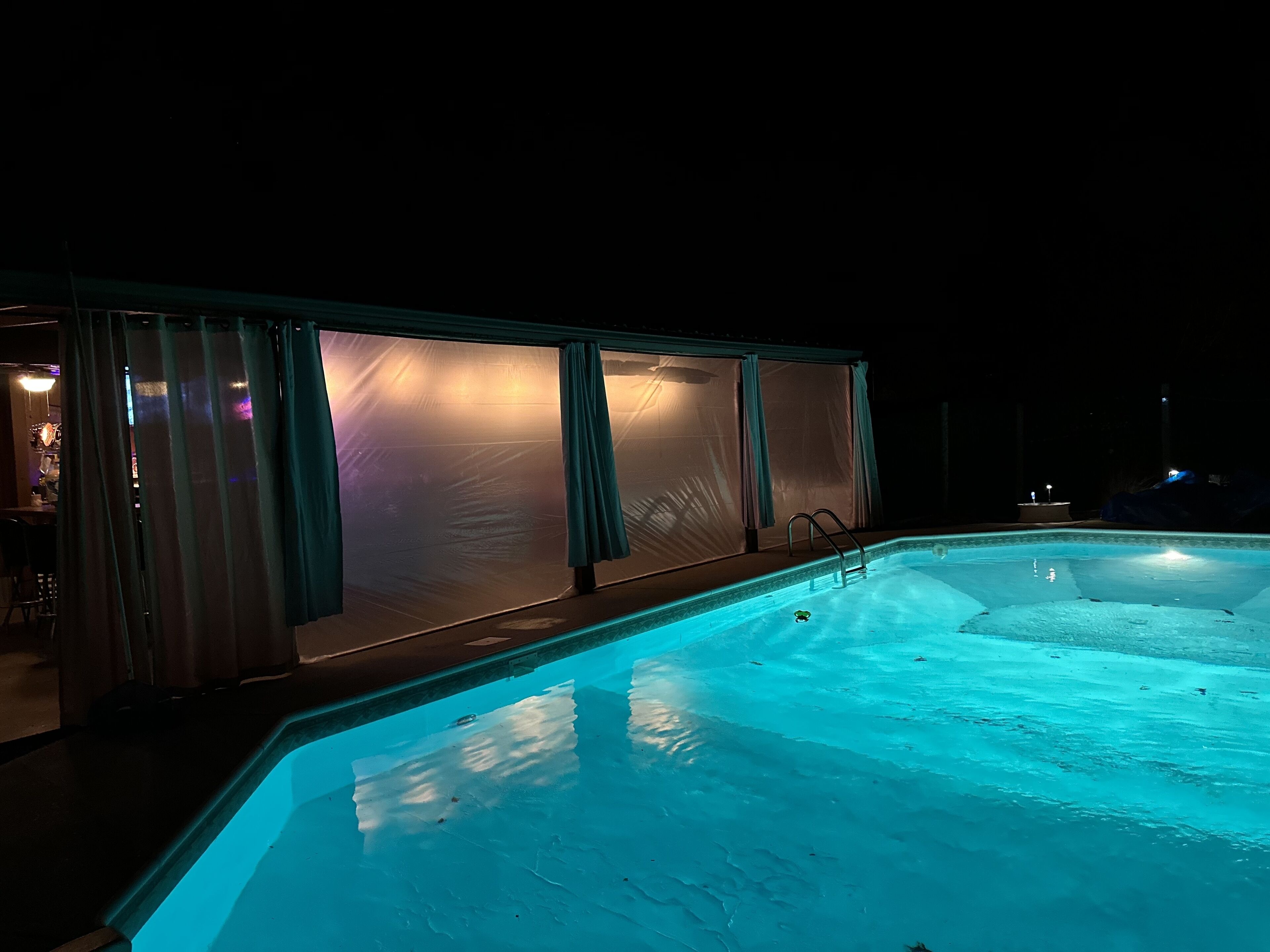 A swimming pool at night with a covered area and a chair.